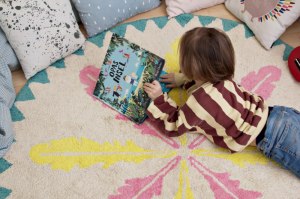 Kind liest auf rundem fair hergestellte Kinderteppich mit Federmotiv von Minividuals Kids Living