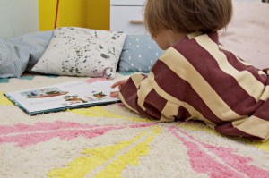Kind liegt auf rundem fair hergestellte Kinderteppich mit Federmotiv von Minividuals Kids Living