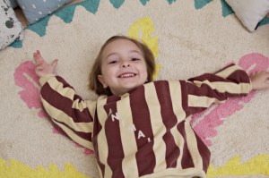 Kind liegt auf rundem fair hergestellte Kinderteppich mit Federmotiv von Minividuals Kids Living