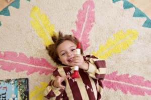 Kind liegt auf rundem, waschbarem Kinderteppich mit Federmotiv von Minividuals Kids Living