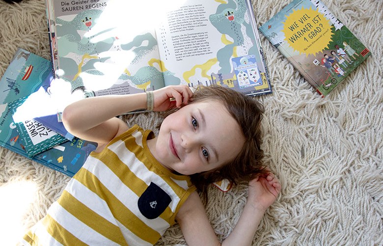 Kind liegt mit Kinderbüchern zum Thema Umweltschutz auf dem Teppich