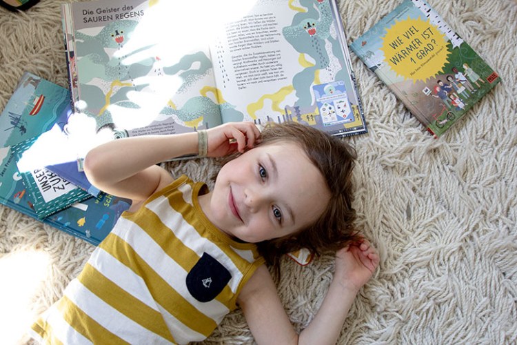Kind liegt mit Kinderbüchern zum Thema Umweltschutz auf dem Teppich
